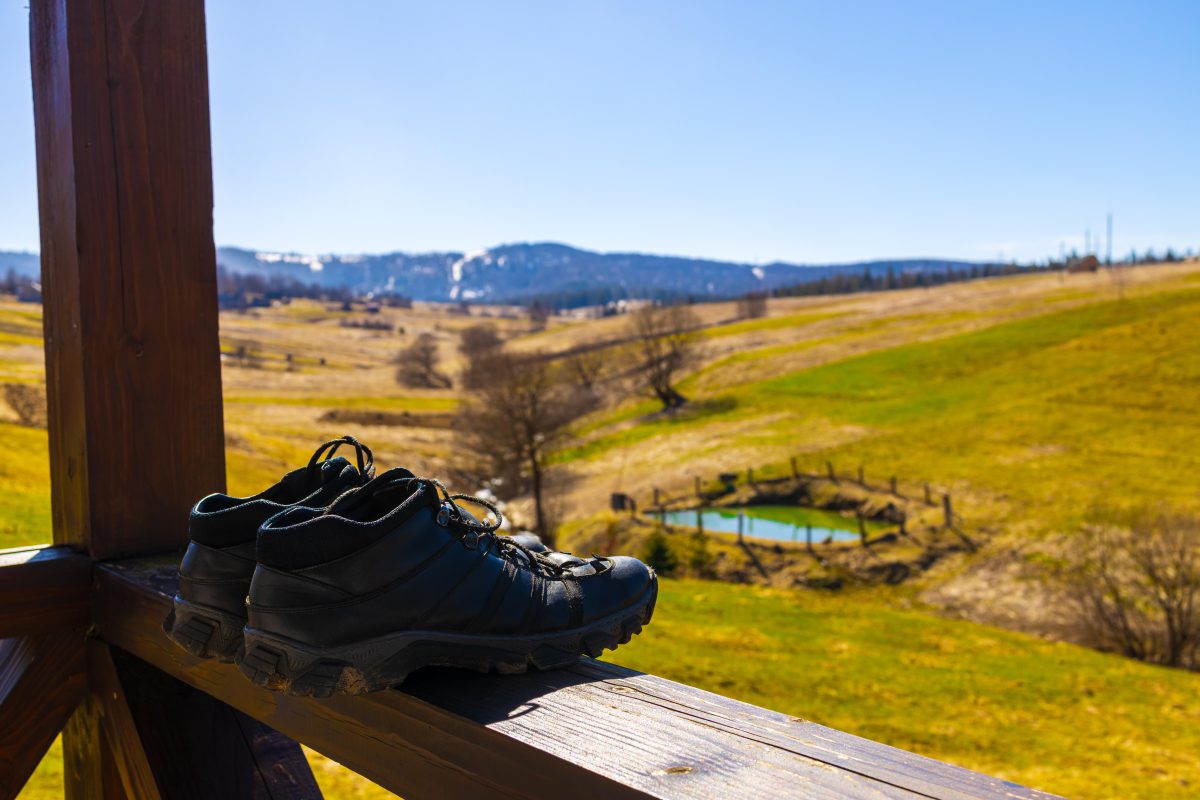 Schuhe nach dem Tragen an die frische Luft stellen – das beugt Feuchtigkeit und unangenehmem Geruch vor Wanderschuhe vor Berghintergrund auf Balkon zum Lüften