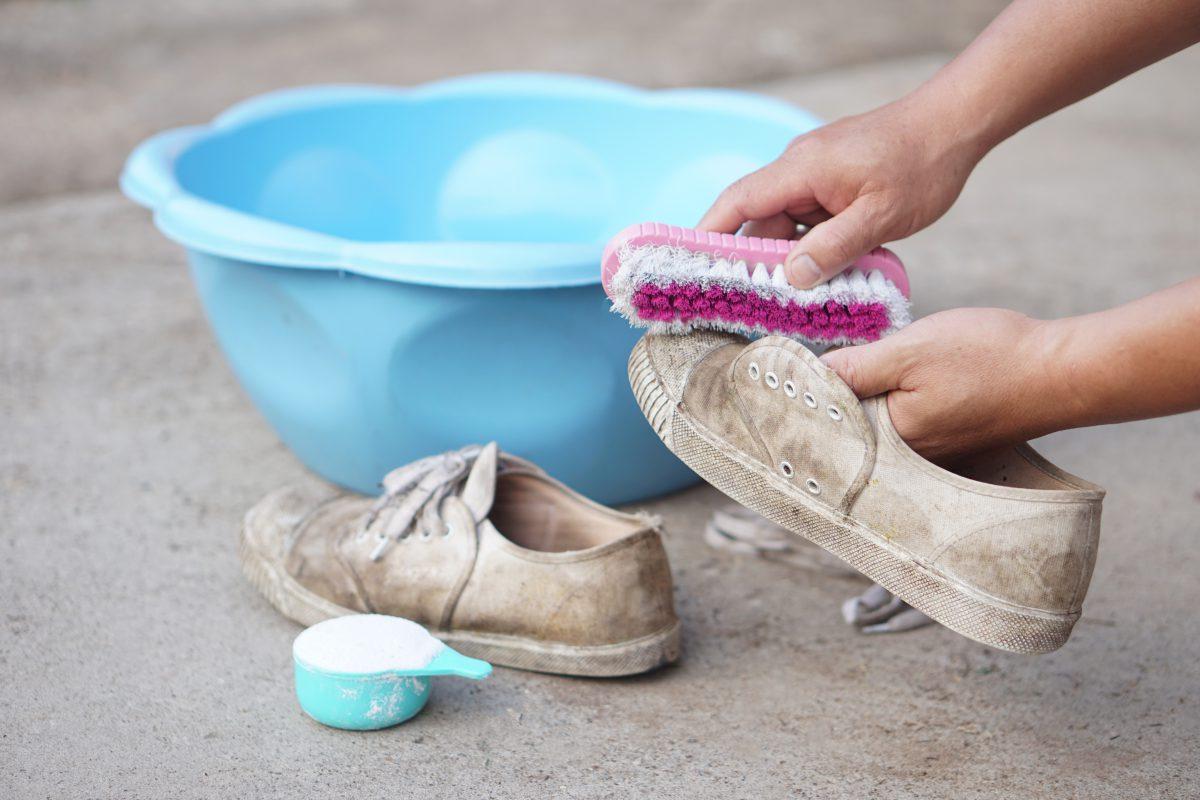 Person bürstet dreckige Schuhe ab. Im Hintergrund ist eine hellblaue Wanne zu sehen - Dürfen Stoffschuhe in die Waschmaschine?